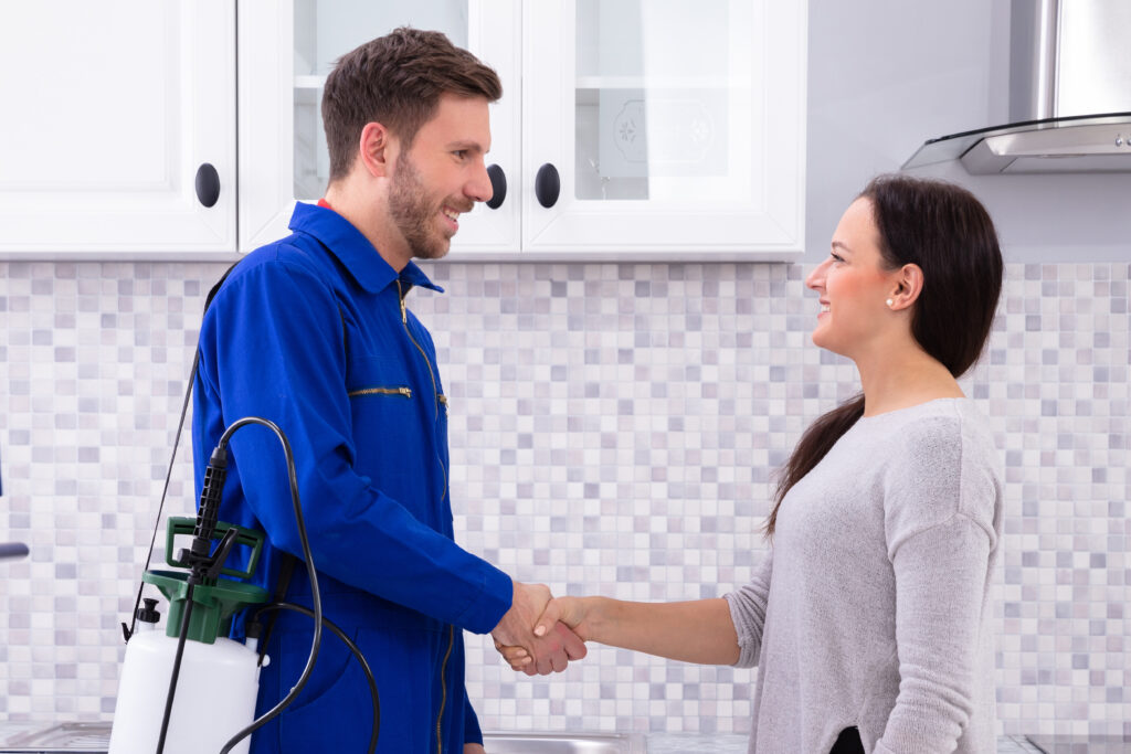 Male Pest Control Worker Shaking Hands With Happy Woman In Kitchen